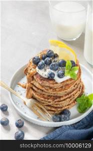 Healthy summer breakfast, homemade classic american pancakes with fresh blue berries, lemon, yogurt and peanut butter. Morning light grey stone background.