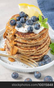 Healthy summer breakfast, homemade classic american pancakes with fresh blue berries, lemon, yogurt and peanut butter. Morning light grey stone background.