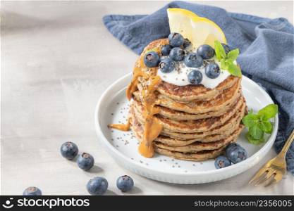 Healthy summer breakfast, homemade classic american pancakes with fresh blue berries, lemon, yogurt and peanut butter. Morning light grey stone background.