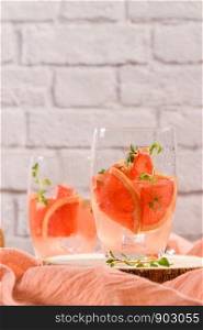 Healthy summer drink grapefruit lemonade with thyme in glasses with ice on a wooden surface.