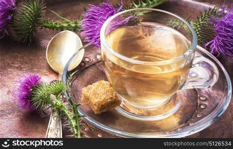 healthy tea with thistle. glass cup on saucer with tea from a medicinal inflorescence thistle