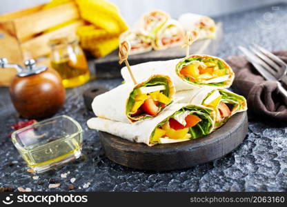 Healthy tortilla wraps viewed from side on wooden cutting board, tortilla with chicken and vegetables