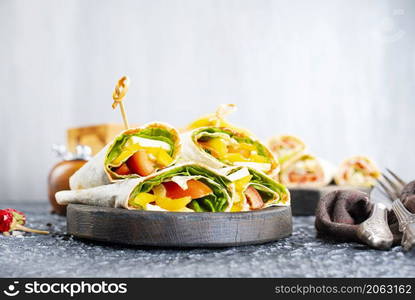 Healthy tortilla wraps viewed from side on wooden cutting board, tortilla with chicken and vegetables