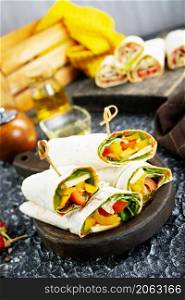 Healthy tortilla wraps viewed from side on wooden cutting board, tortilla with chicken and vegetables
