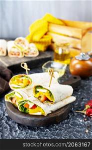 Healthy tortilla wraps viewed from side on wooden cutting board, tortilla with chicken and vegetables