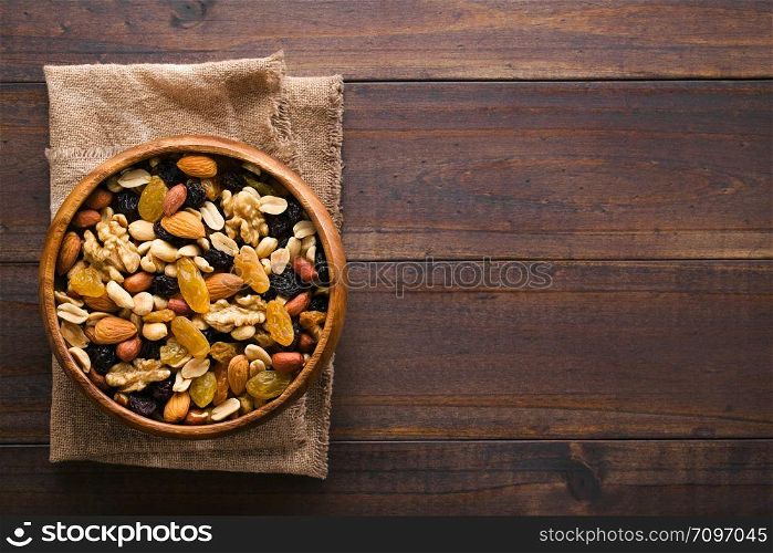 Healthy trail mix snack made of nuts (walnut, almond, peanut) and dried fruits (raisin, sultana) in wooden bowl, photographed overhead with copy space on the right side. Trail Mix Snack of Nuts and Dried Fruits