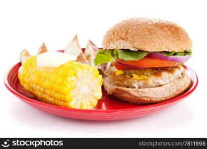 Healthy turkey burger, corn on the cob, and baked potato wedges on white background.