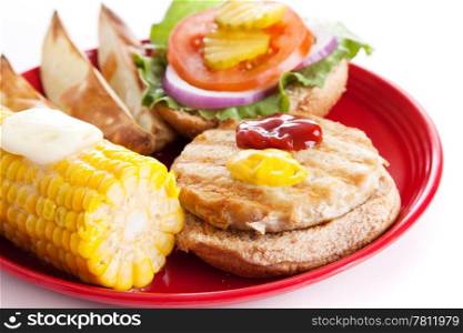 Healthy turkey burger on a whole grain bun, with baked potato wedges and corn on the cob. Isolated on white.