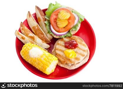 Healthy turkey burger on a whole grain bun, with baked potato wedges and corn on the cob. Isolated with clipping path.