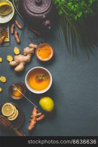 Healthy turmeric spice tea preparation on gray background with teapot, cup of tea,  lemon,  ginger, cinnamon sticks and honey , top view.  Immune boosting remedy , detox and dieting concept