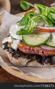 Healthy vegan burger with fresh vegetables and yogurt sauce on rustic kitchen counter top.