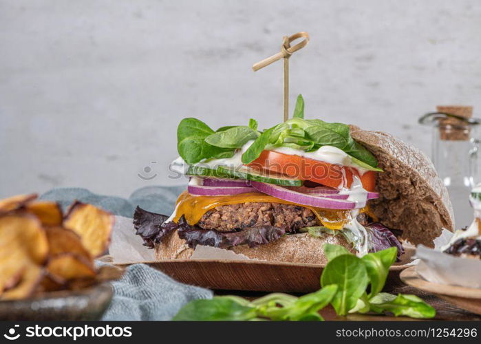 Healthy vegan burger with fresh vegetables and yogurt sauce on rustic kitchen counter top.