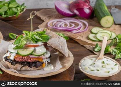 Healthy vegan burger with fresh vegetables and yogurt sauce on rustic kitchen counter top.
