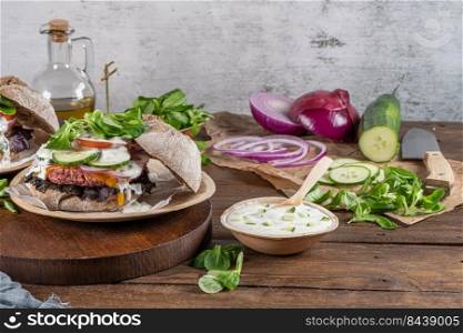 Healthy vegan burger with fresh vegetables and yogurt sauce on rustic kitchen counter top.