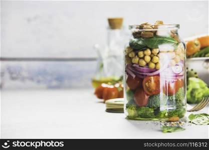Healthy vegan energy boosting salad with chickpeas, broccoli, tomatoes, red onion, spinach and nuts in glass jar, concrete background, selective focus. Clean eating, superfood, vegan, detox food concept