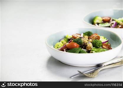 Healthy vegan energy boosting salad with chickpeas, broccoli, tomatoes, red onion, spinach and nuts in blue plate on concrete background, selective focus. Clean eating, superfood, vegan, detox food concept