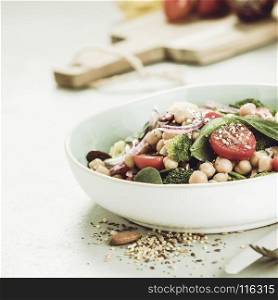 Healthy vegan energy boosting salad with chickpeas, broccoli, tomatoes, red onion, spinach and nuts in blue plate on concrete background, selective focus. Clean eating, superfood, vegan, detox food concept