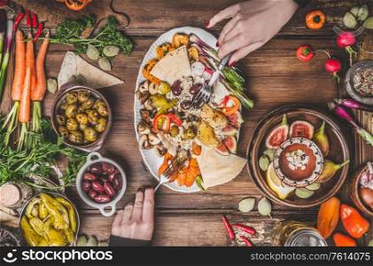 Healthy vegan food with hummus plate. Female hands holding tasty snack on kitchen tables. Ramadan iftar dinner. Various pickled and fresh vegetables. Mediterranean cuisine