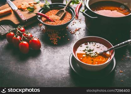 Healthy vegan lentil soup in bowl with spoon on dark kitchen table background with ingredients. Vegetarian food. Clean diet eating. Source of plant based protein