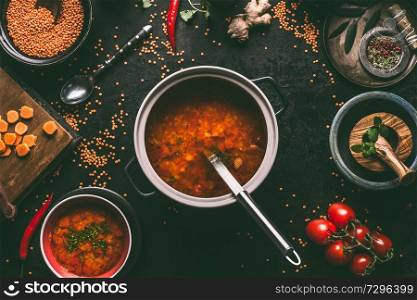 Healthy vegan lentil soup in cooking pot with ladle on dark kitchen table background with ingredients. Vegetarian food. Clean diet eating. Source of plant based protein