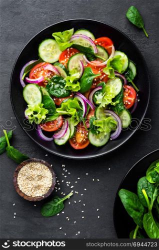 Healthy vegetable salad of fresh tomato, cucumber, onion, spinach, lettuce and sesame on plate. Diet menu. Top view.