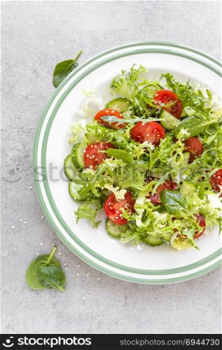 Healthy vegetable salad of fresh tomato, cucumber, spinach, frize and sesame on plate. Diet menu. Top view.