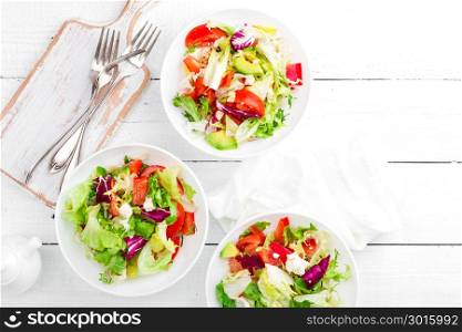 Healthy vegetable salad with fresh greens, lettuce, avocado, tomato, seet pepper and goat cheese. Delicious and nutritious diet dish for breakfast. Salad bowls on white wooden background. Overhead view
