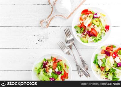 Healthy vegetable salad with fresh greens, lettuce, avocado, tomato, seet pepper and goat cheese. Delicious and nutritious diet dish for breakfast. Salad bowls on white wooden background. Top view