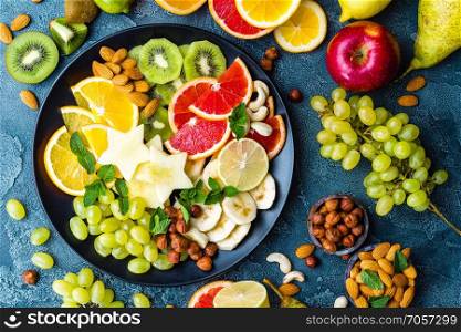 Healthy vegetarian bowl dish with fresh fruits and nuts. Plate with raw apple, orange, grapefruit, banana, kiwi, lemon, grape, almond, hazelnut and cashew nuts. Healthy balanced eating