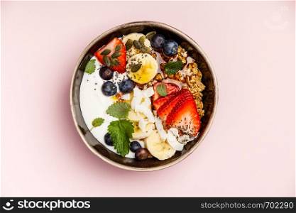 Healthy vegetarian breakfast- Oat granola with fresh berries, banana, yogurt, maple syrup, seeds and mint leaves on pink background, flat lay, top view. Healthy breakfast set on pink background, top view, copy space