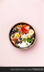 Healthy vegetarian breakfast- Oat granola with fresh berries, banana, yogurt, maple syrup, seeds and mint leaves on pink background, flat lay, top view
