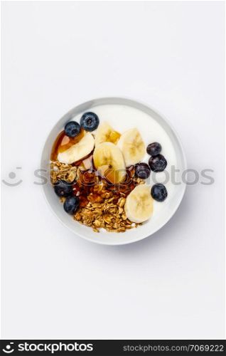 Healthy vegetarian breakfast- Oat granola with fresh blueberries, banana, soy yogurt and maple syrup on white background, flat lay, top view