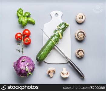 Healthy vegetarian clean food concept with vegetables cooking ingredients: cutting board and knife on gray background, top view, flat lay