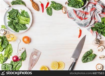 Healthy vegetarian cooking with spinach leaves on white wooden background with kitchen knife and ingredients, top view frame. Vegan or diet food concept