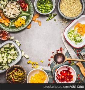 Healthy vegetarian dish preparation with Diced feta cheese, cut vegetables in bowls, pearl barley , cooking spoon and kitchen knife, top view. Clean Diet nutrition concept