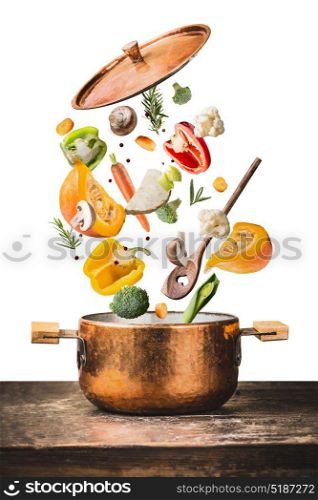 Healthy vegetarian eating and cooking with various flying chopped vegetables ingredients, cooking pot and spoon at wooden table desk , isolated on white background, front view. Clean food concept