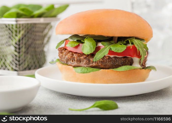 Healthy vegetarian meat free burger on round ceramic plate with vegetables and spinach on light background..