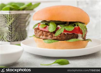 Healthy vegetarian meat free burger on round ceramic plate with vegetables and spinach on light background..