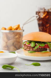 Healthy vegetarian meat free burger on round ceramic plate with vegetables on light background with potato wedges and glass of cola.