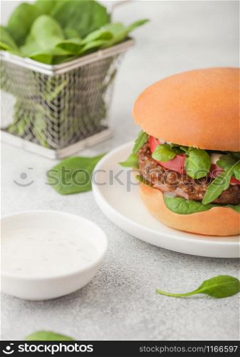 Healthy vegetarian meat free burger on round chopping board with vegetables and spinach on light background. Top view