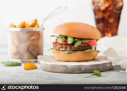 Healthy vegetarian meat free burger on round chopping board with vegetables on light background with potato wedges and glass of cola.