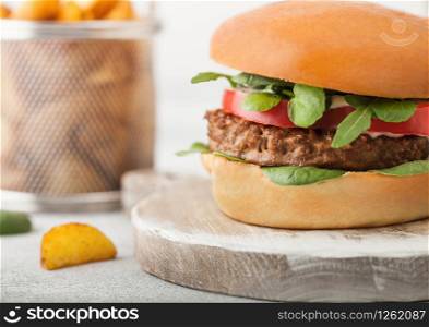 Healthy vegetarian meat free burger on round chopping board with vegetables on light background with potato wedges.