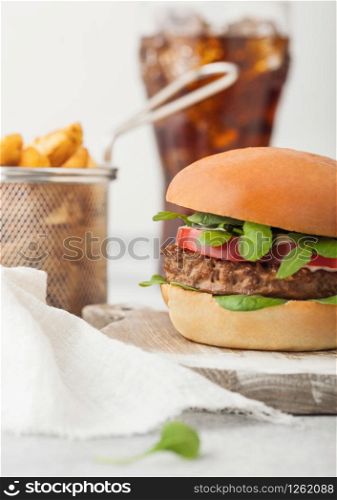 Healthy vegetarian meat free burger on round chopping board with vegetables on light background with potato wedges and glass of cola.