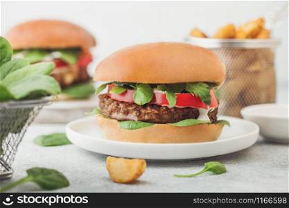 Healthy vegetarian meat free burgers on round ceramic plate with vegetables on light background with potato wedges and fresh spinach.