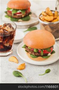 Healthy vegetarian meat free burgers on round ceramic plate with vegetables on light background with potato wedges and glass of cola.