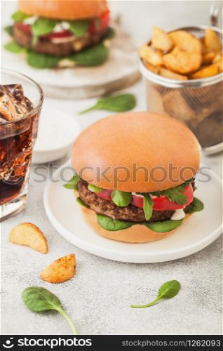 Healthy vegetarian meat free burgers on round ceramic plate with vegetables on light background with potato wedges and glass of cola.