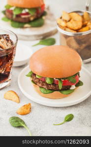 Healthy vegetarian meat free burgers on round ceramic plate with vegetables on light background with potato wedges and glass of cola.