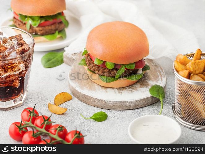 Healthy vegetarian meat free burgers on round chopping board with vegetables on light background with potato wedges and glass of cola and cherry tomatoes.