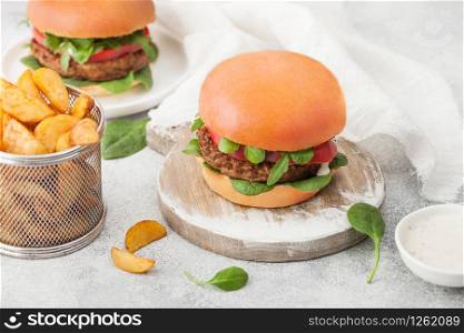 Healthy vegetarian meat free burgers on round chopping board with vegetables on light background with potato wedges.