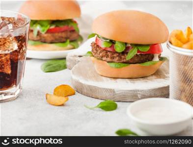 Healthy vegetarian meat free burgers on round chopping board with vegetables on light background with potato wedges and glass of cola.